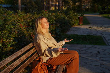 Young woman sitting on park bench and enjoying the sun rays, relaxing with eyes closed             