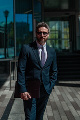 Handsome millennial business man standing outdoor on modern office building. Business success. Business man thinking outdoor. Modern businessman in full suit standing outdoors near office cityscape.