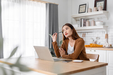 Asian young woman seriously working on computer laptop in house. She thinking find solution problem...