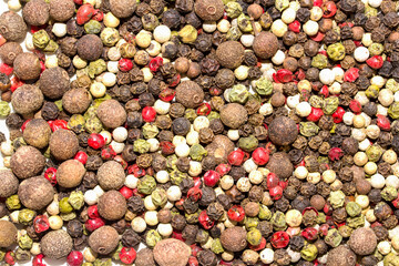 A bunch of different colored pepper seeds are scattered on a white background