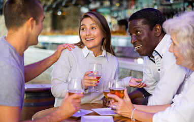 Happy friends cheering and drinking beer at in beer pub indoor. Main focus right in center