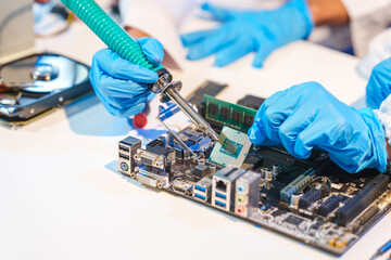 Close-up of a technician wearing gloves soldering electronic components at a desk in an office. The...