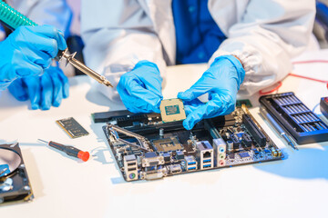Close-up of a technician wearing gloves soldering electronic components at a desk in an office. The...