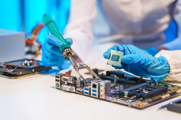 Close-up of a technician wearing gloves soldering electronic components at a desk in an office. The scene highlights precision, technical expertise, and focused work in an electronics lab setting