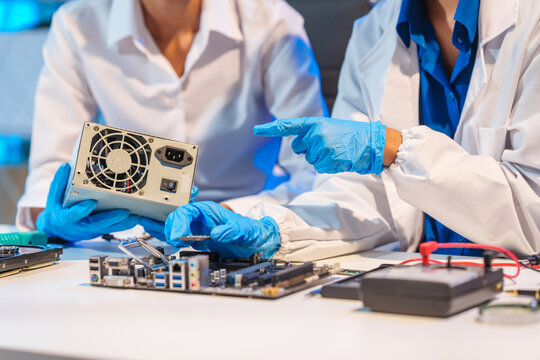Close-up of a technician wearing gloves soldering electronic components at a desk in an office. The scene highlights precision, technical expertise, and focused work in an electronics lab setting