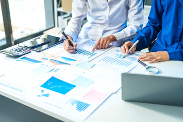 Two Asian business woman working and talking at a table with documents, a graph, and a digital tablet. They are focused on analysis, business planning, and collaborative discussions