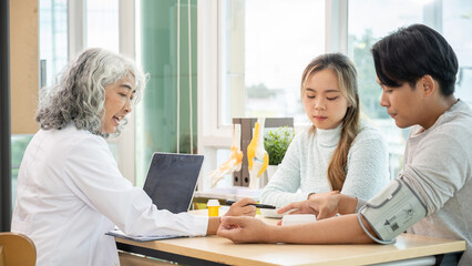 Obraz premium A professional senior Asian female doctor in a uniform having a consultation with a young married couple in the examination room. doctor visit, health care, medical