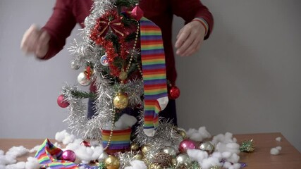 A cozy setup showcasing hands decorating a small Christmas tree with glittering baubles and rainbow-inspired accessories. An inclusive holiday celebration