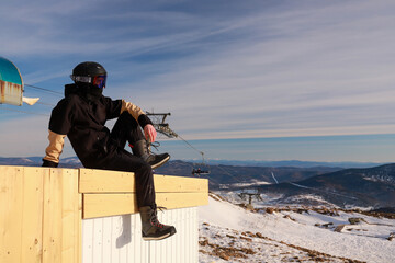 man in black snowboard suit sits against mountains enjoying view