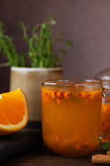 Sea buckthorn tea with orange, cinnamon, honey and thyme in glass on a brown table, closeup. Herbal vitamin tea. Hot autumn drink. Vertical orientation.