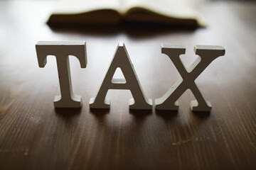 Wooden Letters Spelling Tax with Blurred Open Book Background on Wooden Table