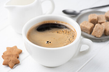 Cup of black coffee served in white porcelain cup with stars shaped cookies and brown sugar