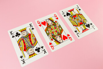 Top view of playing cards on pink background. King, queen and jack cards. Three cards, board game, poker. Copy space, flat lay.