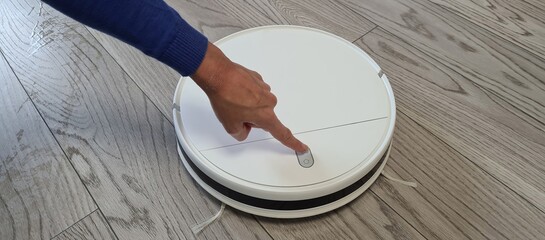 Female finger pressing power button on white robotic vacuum cleaner