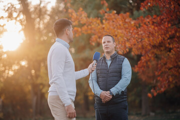 Journalist interviewing businessman in autumn park at sunset