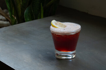 Iced cold brew coffee with cranberry and sliced lime mocktail, served in a transparent glass, placed over concrete surface