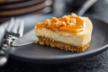 A cut piece of cheesecake with caramel topping on plate on black table.