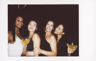 A joyful group of friends pose together while holding cocktails, captured in a vintage-style instant photo. The image has a nostalgic, dusty look with scratches enhancing the retro feel.