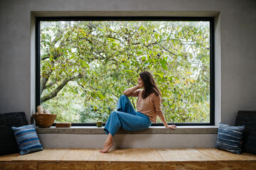 Beautiful woman sitting in front of large window, clean space.