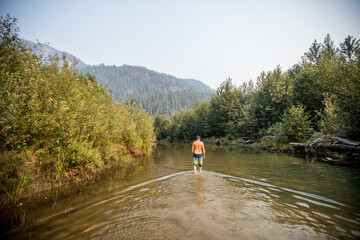 First Nations man wading in shallow river, connecting to the land