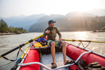 Guide rowing red raft on river at sunrise