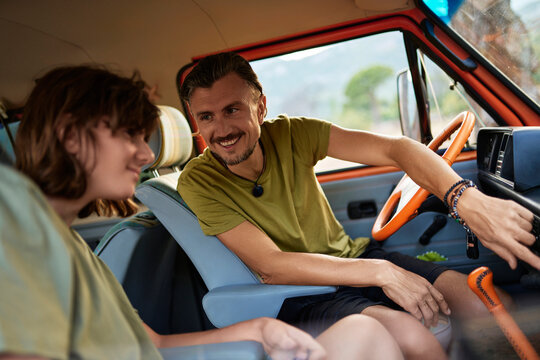 Smiling man teaching his teenage son how to drive caravan