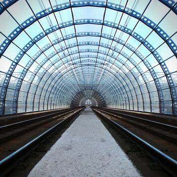 View of two railway tracks from the middle of a concrete walkway in a glass train station tunnel