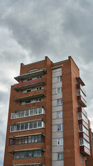 Fototapeta premium The facade of a modern multi-storey red brick building. An apartment building on the background of clouds. The concept of mortgage lending. Buying an apartment.