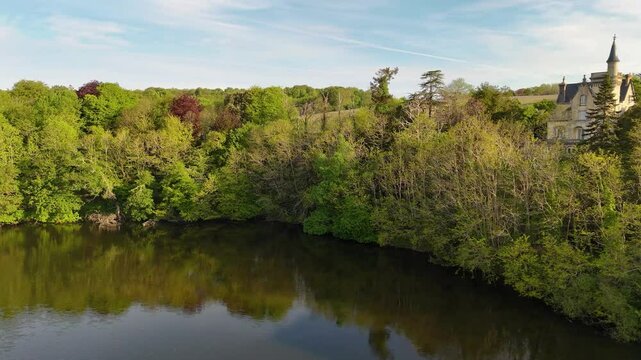 Drone view Moros Lagoon, Concarneau, France, showing calm waters mand small castle, lush trees, vibrant blue sky with clouds, ideal for nature, relaxation, travel projects.