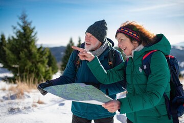 Older tourist using map during their hike in snowy winter mountains. Elderly couple in winter nature.