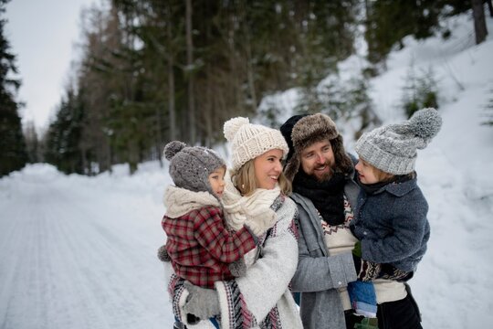 Rear view of family is enjoying winter holiday in the mountains, holding hands while walking through the snowy forest.
