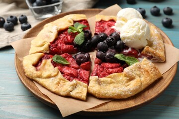 Tasty galette with berries, ice cream and mint on light blue wooden table, closeup