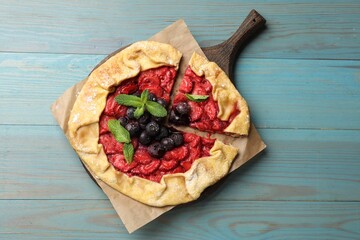 Tasty galette with strawberries, blueberries and mint on light blue wooden table, top view