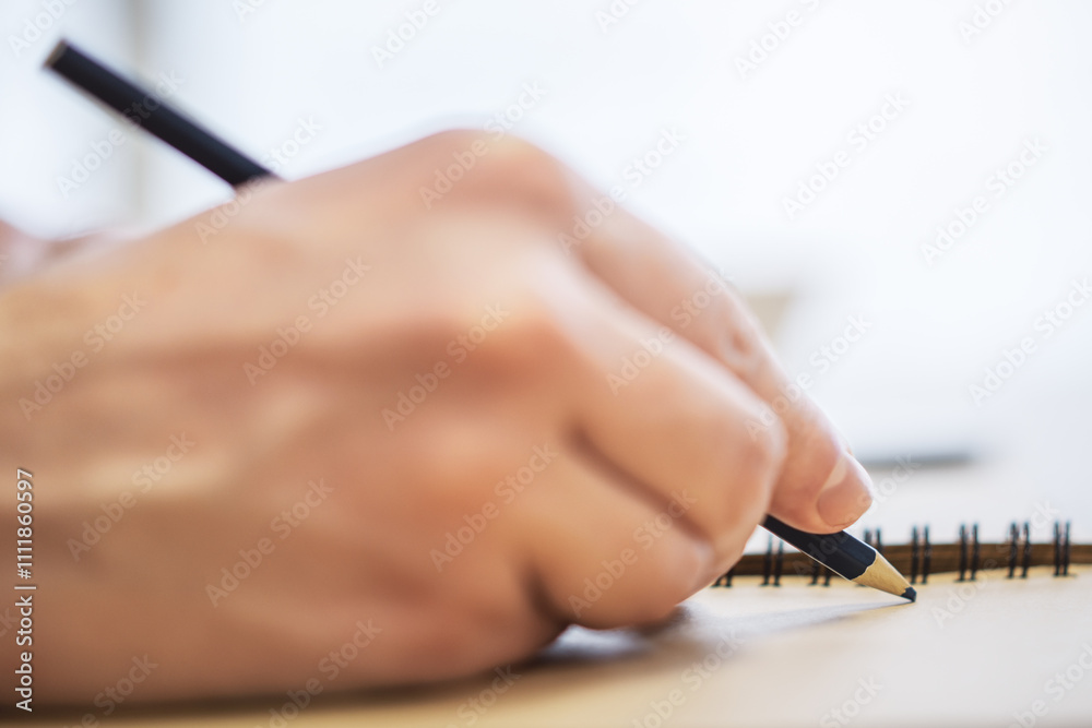 Aufkleber Close perspective of a man's hand making entries in a notepad, with a soft blur in the surrounding