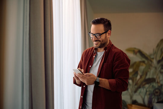 Happy man texting on cell phone by window.