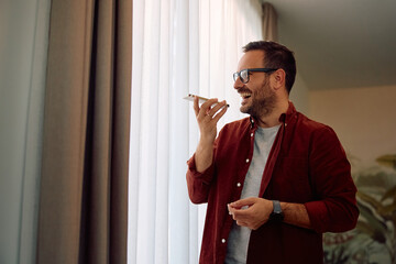 Happy man talking over smart phone's speaker at home.