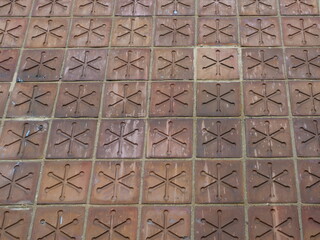 Square reddish clinker paving with a diagonal cross pattern creates a decorative traffic area, standing out with its symmetrical design.