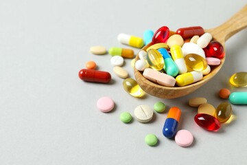 Various medicine pills and capsules in spoon on gray background 