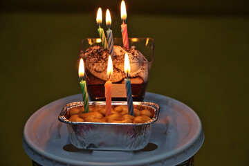 Candles are lit on a cake in a small square container.