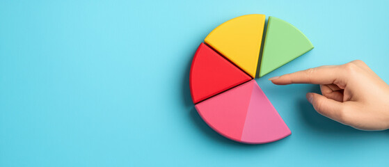 Obraz premium hand pointing at colorful pie chart on blue background, showcasing vibrant segments in red, yellow, green, and pink. This represents data visualization and analysis
