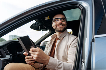 Confident Hispanic man holding digital tablet, using mobile app or navigator in modern new car
