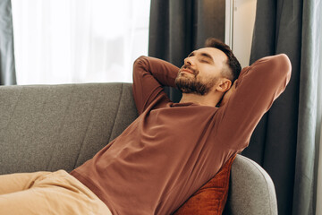 Fototapeta premium Smiling, handsome Hispanic man relaxing, lying on comfortable sofa in cozy home. Resting concept