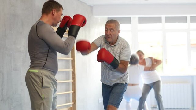 Coach and senior man pupil are engaged during training, boxing classes. Male trainer helps student to work out force of blow, to box quickly and effectively 