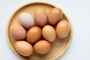 Six brown eggs in a wooden bowl on a white surface. A plate of eggs with a gray background. Eggs plate gray background lies tree. A plate of eggs lies on lifestyle a tree.
