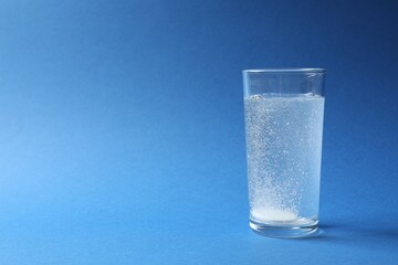 Effervescent pill dissolving in a glas water on blue background 