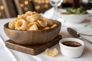 Golden brown pork rinds in rustic wooden bowl overflowing with crispy, savory dipping sauce nearby