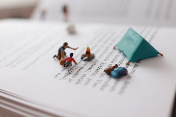 Miniature, micro people. Camping on a page of a book. Father and son burning down a fire.