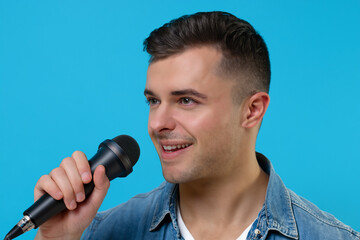 Naklejka premium A man is singing into a microphone. A guy in blue microphone with a blue background. Guy microphone blue background boy sing music. Boy singing music in a microphone lifestyle.