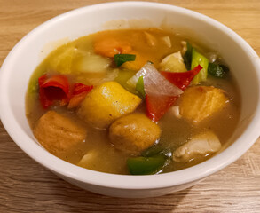 Close up of Sapo tahu or clay pot tofu, Indonesian Chinese tofu dish in white bowl isolated on wooden background.