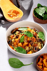 A vegan risotto with roasted pumpkin, mushrooms, and fresh spinach served in a white bowl on a light background